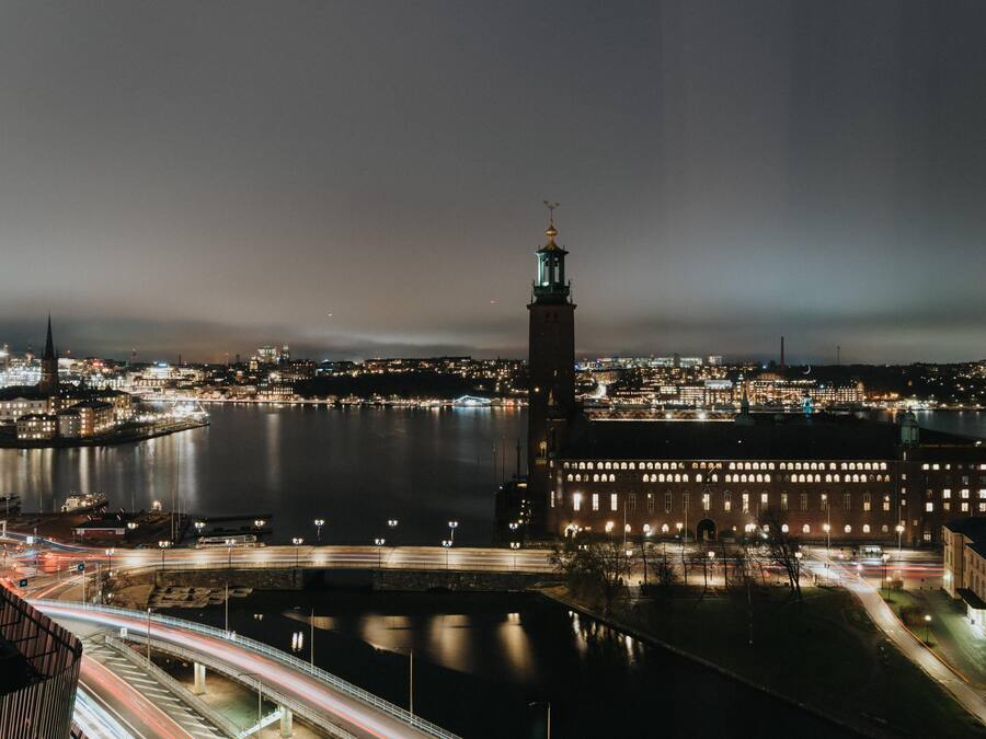 Un paisaje urbano nocturno con una torre destacada y un cuerpo de agua que refleja las luces de la ciudad.