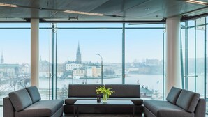 Moderni sisustus, jossa on sohvaryhmä ja sohvapöytä sekä suuret ikkunat, joista avautuu näkymä kaupunkiin.