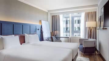 A hotel room with a large bed, a desk, a chair, and a view of buildings through the window.