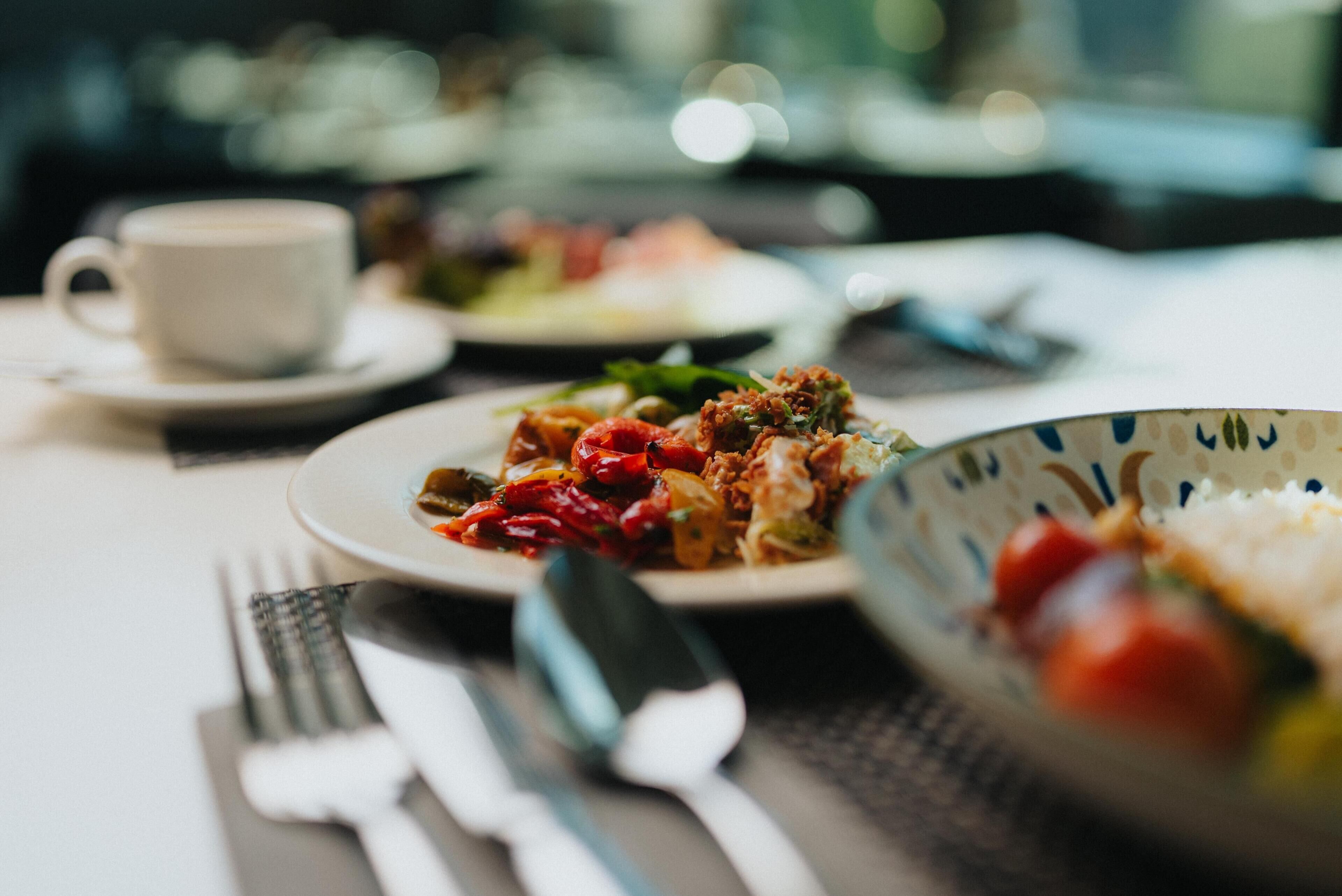 A dining table with plates of food, cutlery, and a cup.