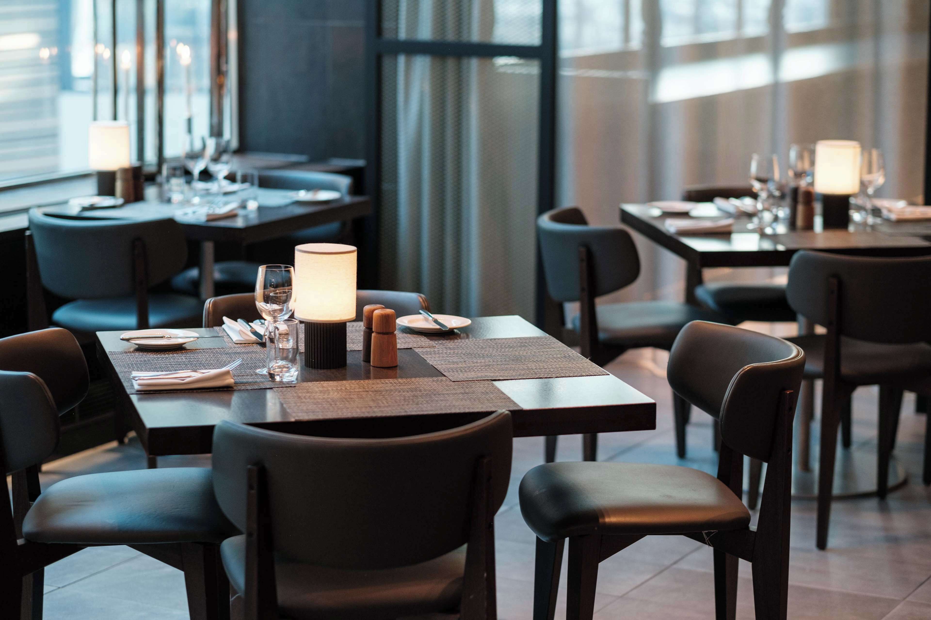 Un restaurante moderno con mesas y sillas de madera oscura, cuidadosamente dispuestas con platos, vasos y cubiertos.