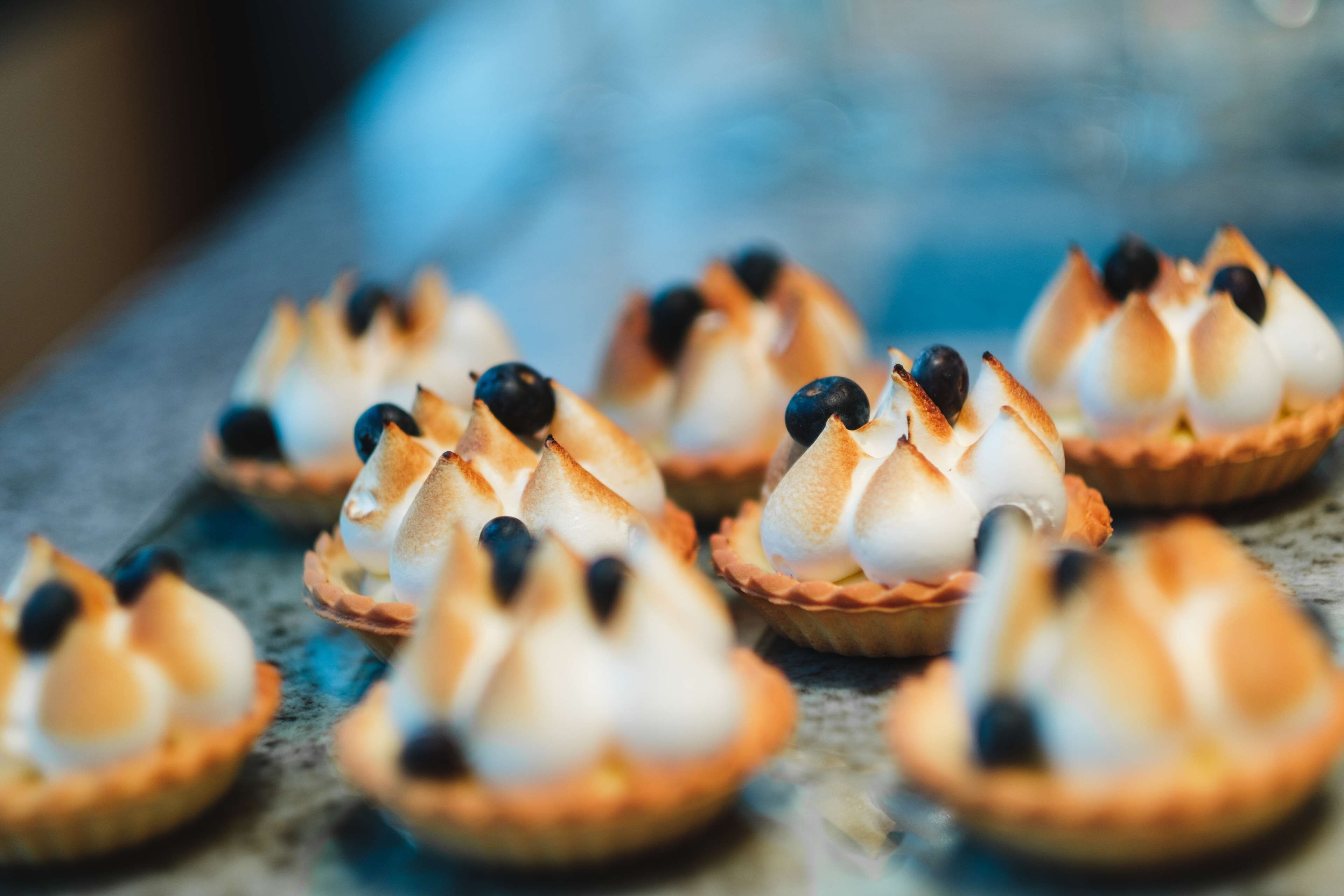 A tray of mini desserts with meringue peaks and blueberries.