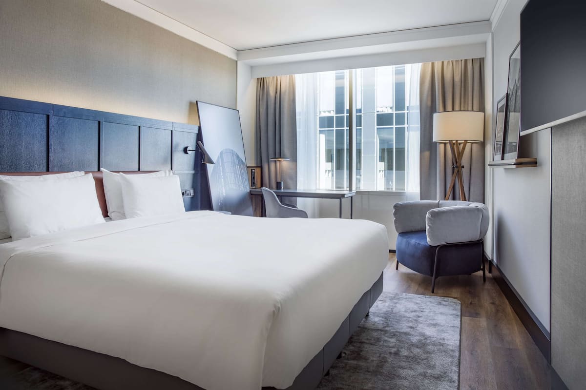 Una camera d'albergo con un letto grande, una scrivania, una sedia e una finestra con tende.