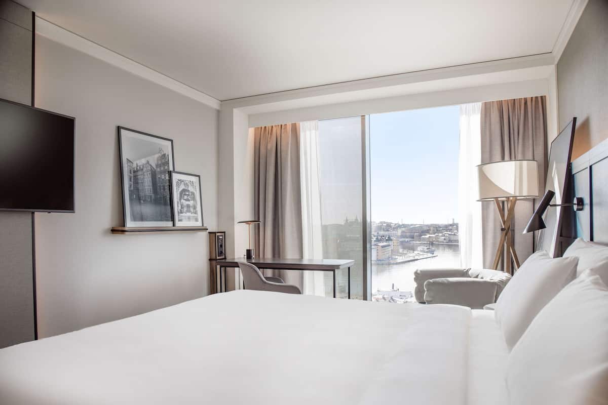 Camera d'albergo con un letto grande, una scrivania, una sedia, una televisione e una finestra con vista sulla città.