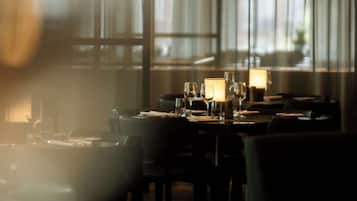En restaurang med dämpad belysning, där borden är dukade för middag, och som präglas av en ombonad atmosfär och stora fönster.