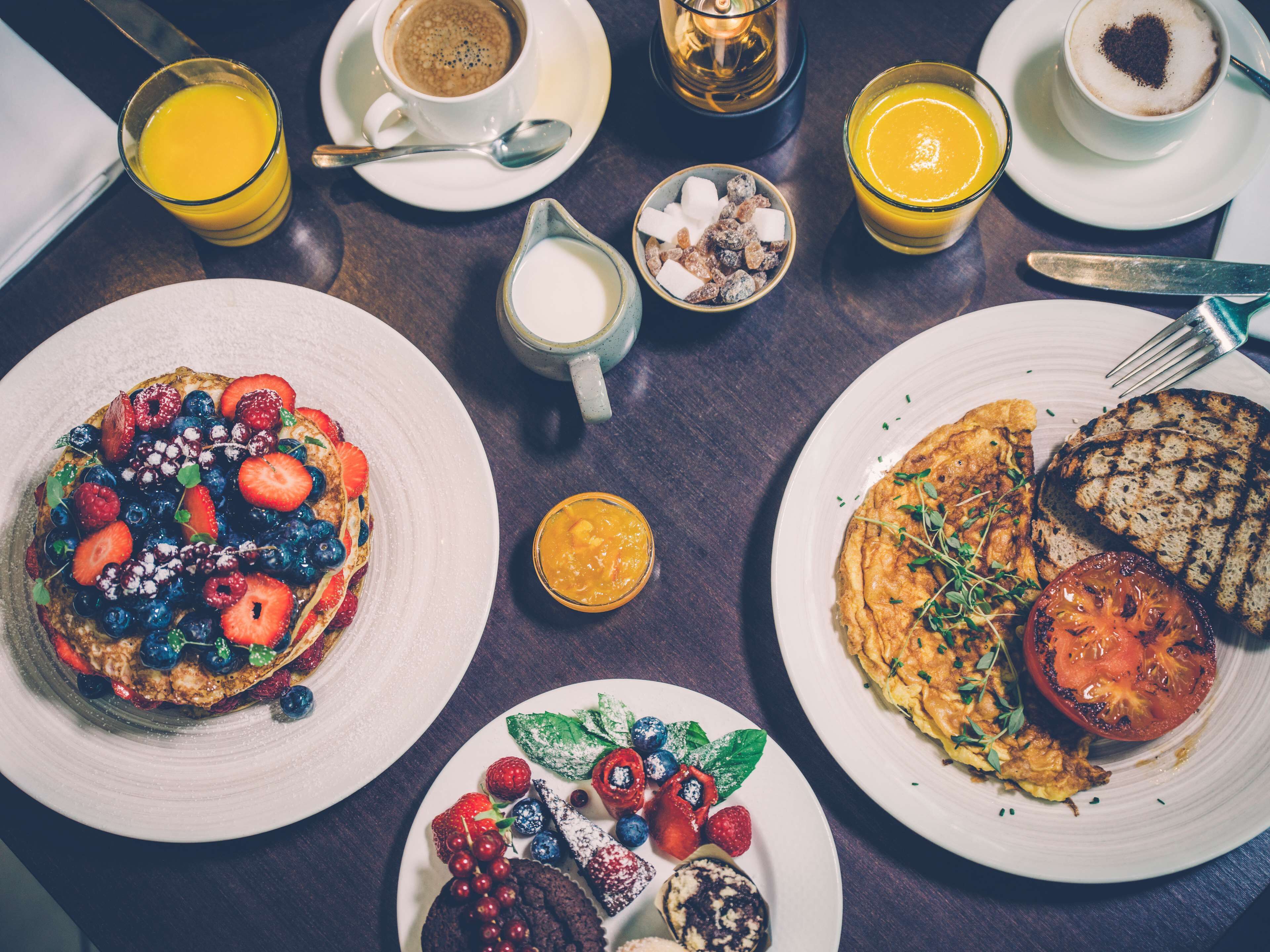 A breakfast table with various dishes including pancakes, toast, and fruit.