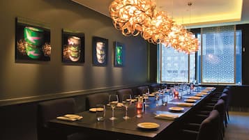 A long dining table set with chairs, a decorative hanging light fixture, and framed artwork on the wall.