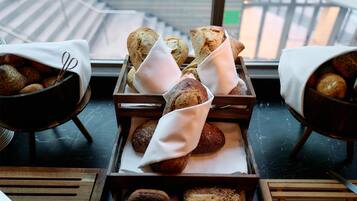 Une vitrine de boulangerie présentant diverses sortes de pains et de pâtisseries, disposés sur des plateaux et recouverts de nappes blanches.