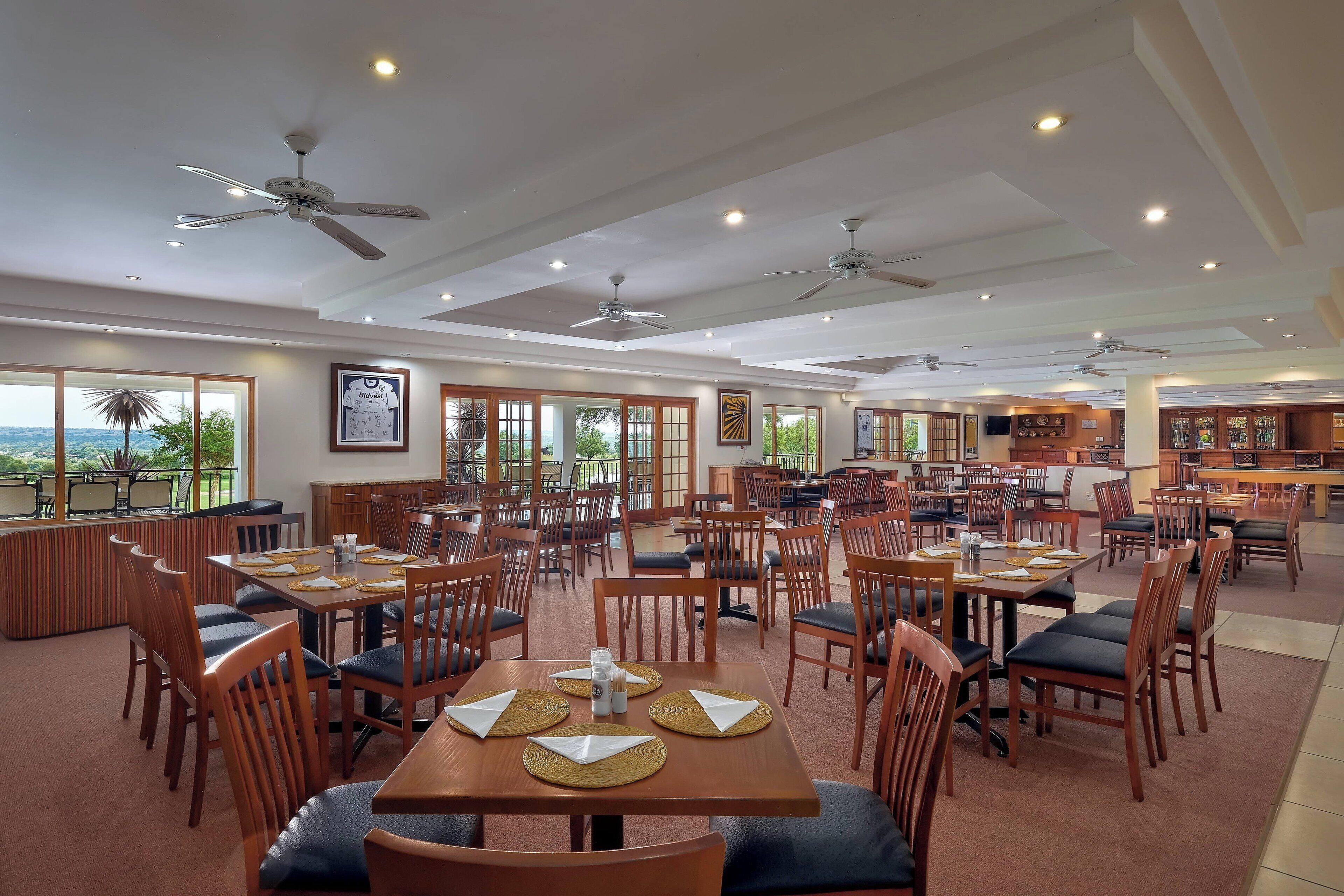 A spacious dining area with multiple tables and chairs, ceiling fans, and large windows offering a view.