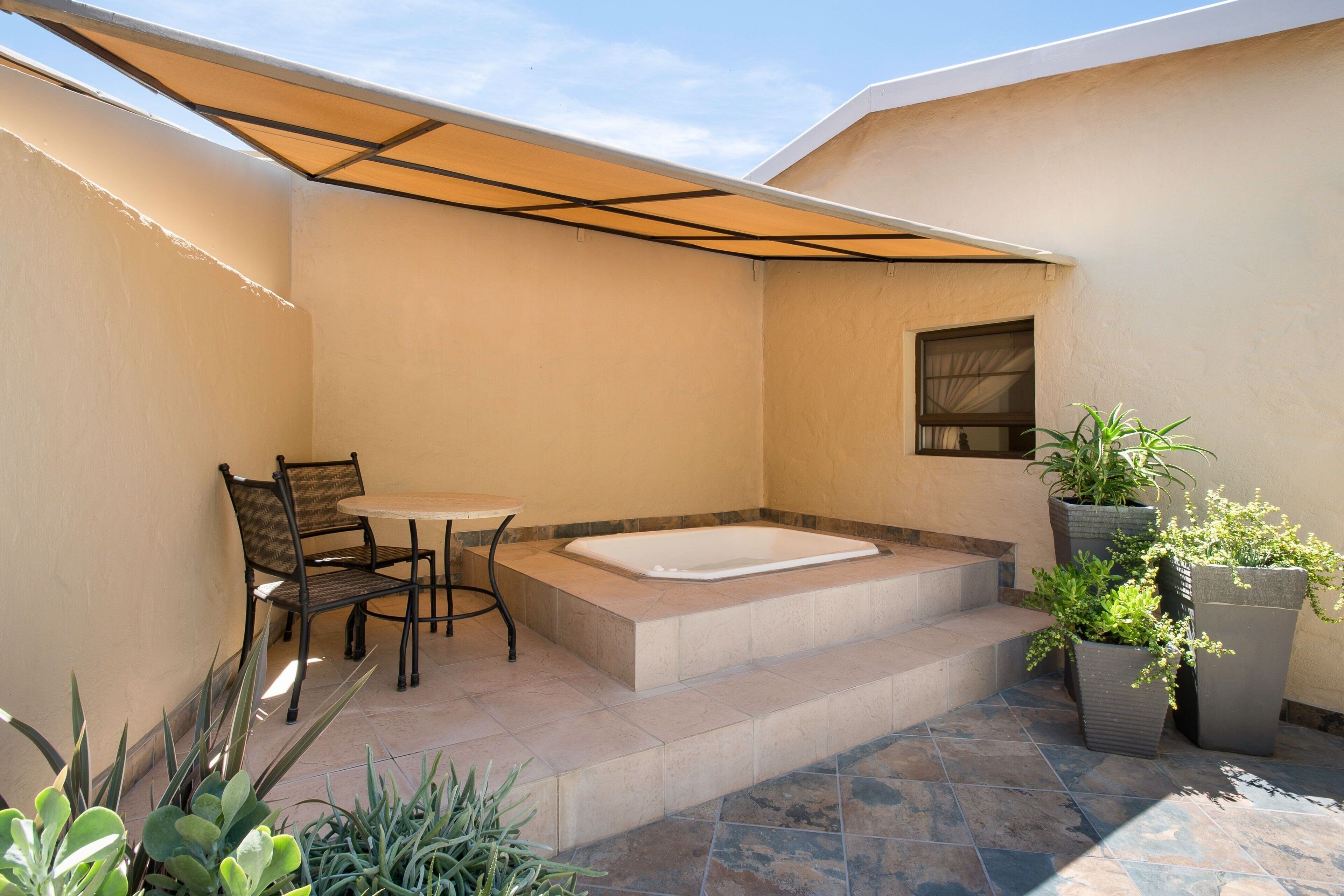 A patio with a hot tub, a table, and chairs, surrounded by potted plants.