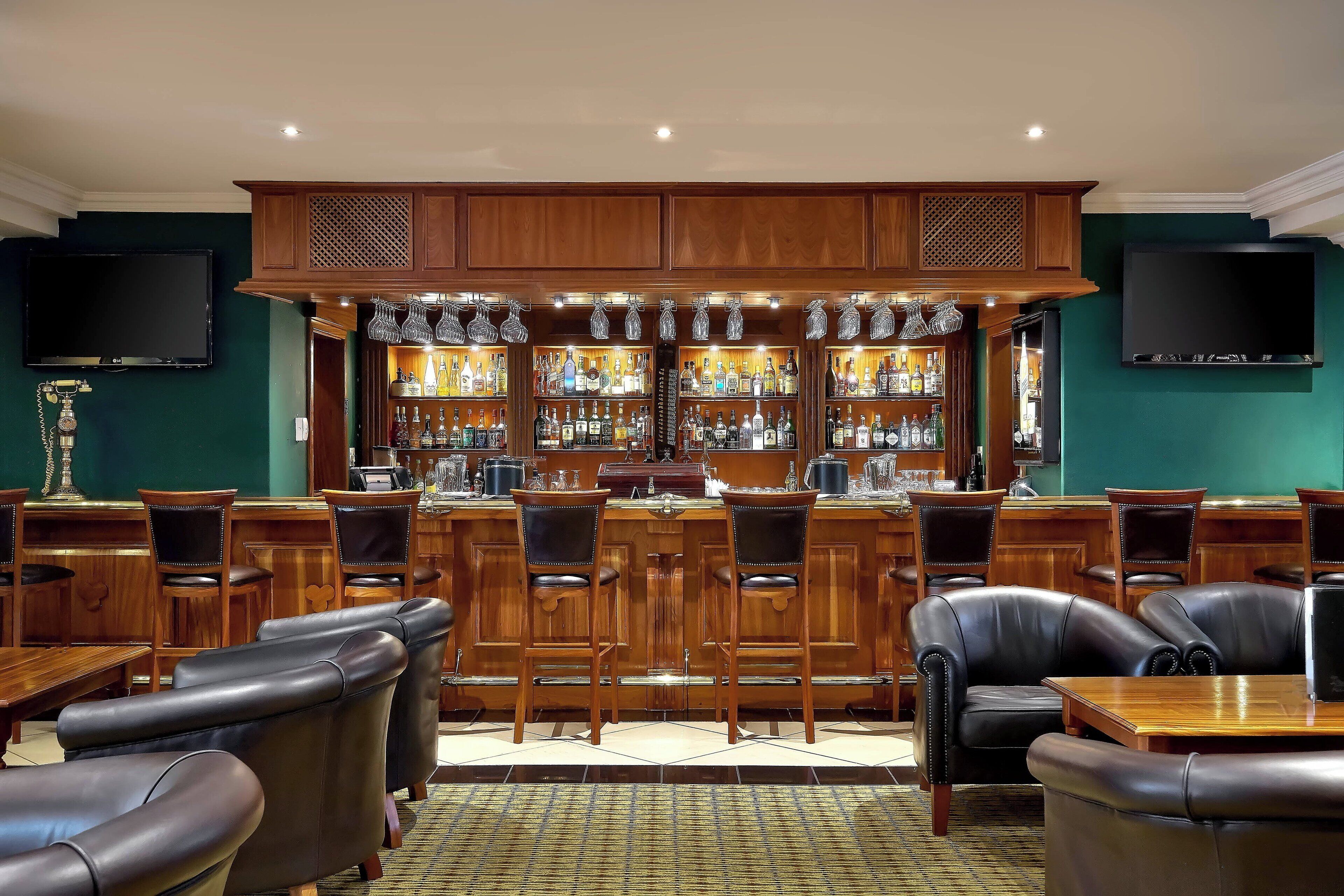 A bar area with wooden cabinets, bar stools, and a variety of bottles.