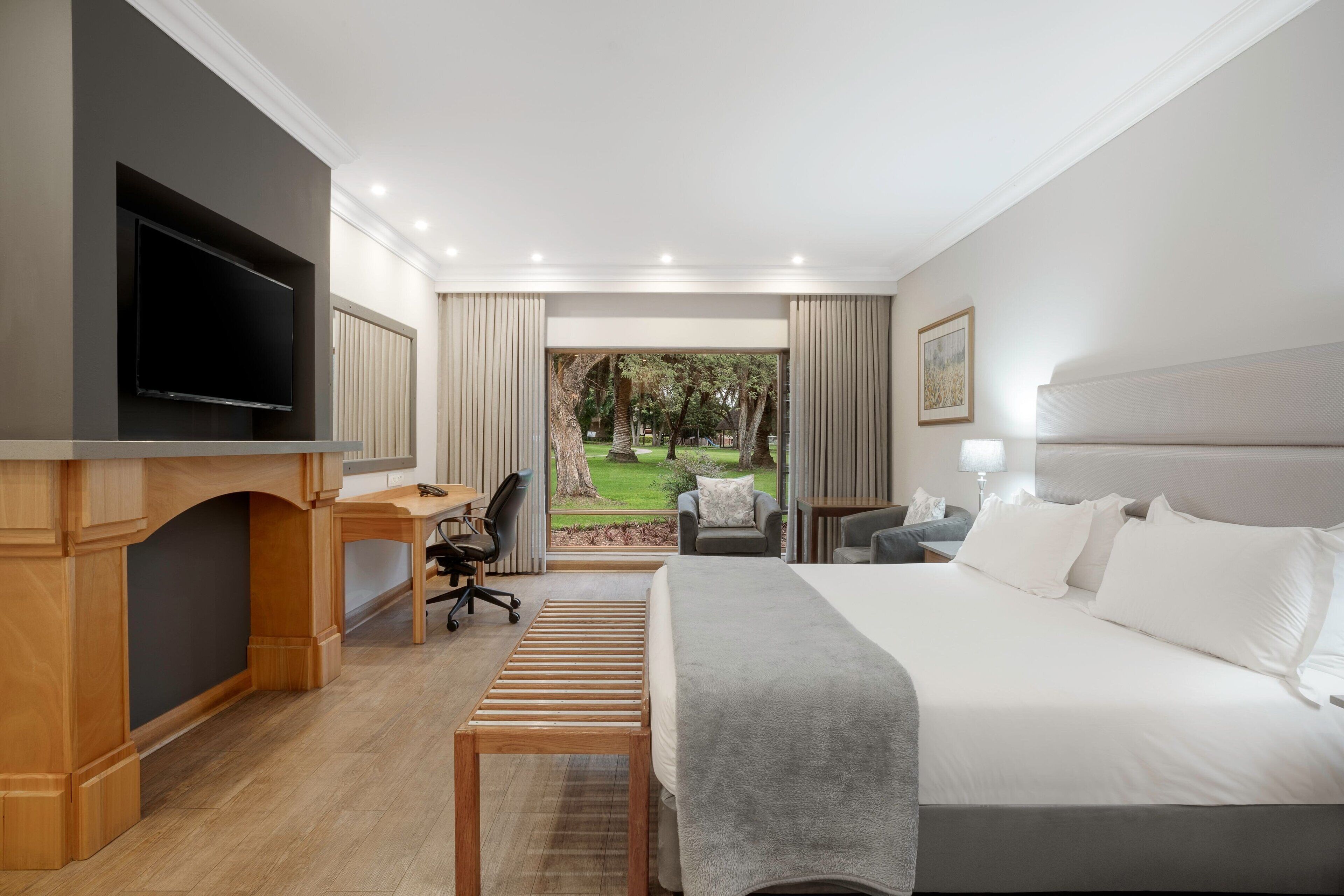 Een moderne hotelkamer met een groot bed, een bureau met stoel, een televisie en uitzicht op een tuin.