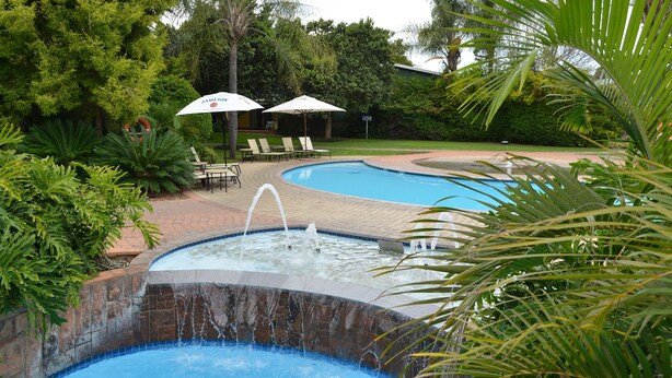 A swimming pool with a water fountain, surrounded by lush greenery and lounge chairs. - Protea Hotel by Marriott Polokwane Ranch Resort (Polokwane)