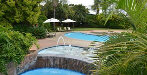 A swimming pool with a water fountain, surrounded by lush greenery and lounge chairs.