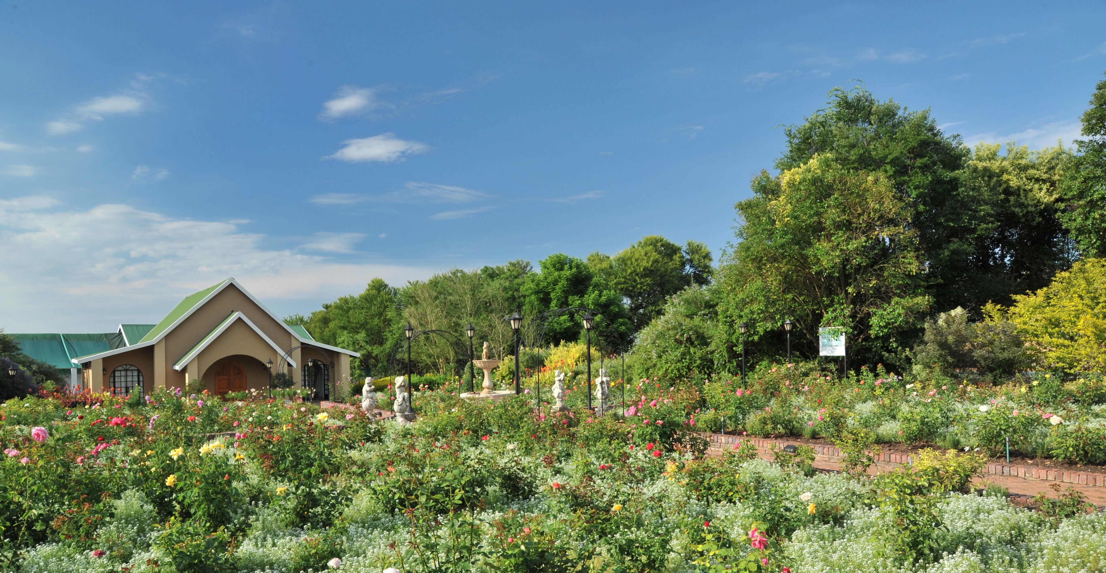 A garden with a variety of flowers and trees, a building with a green roof, and a clear blue sky.