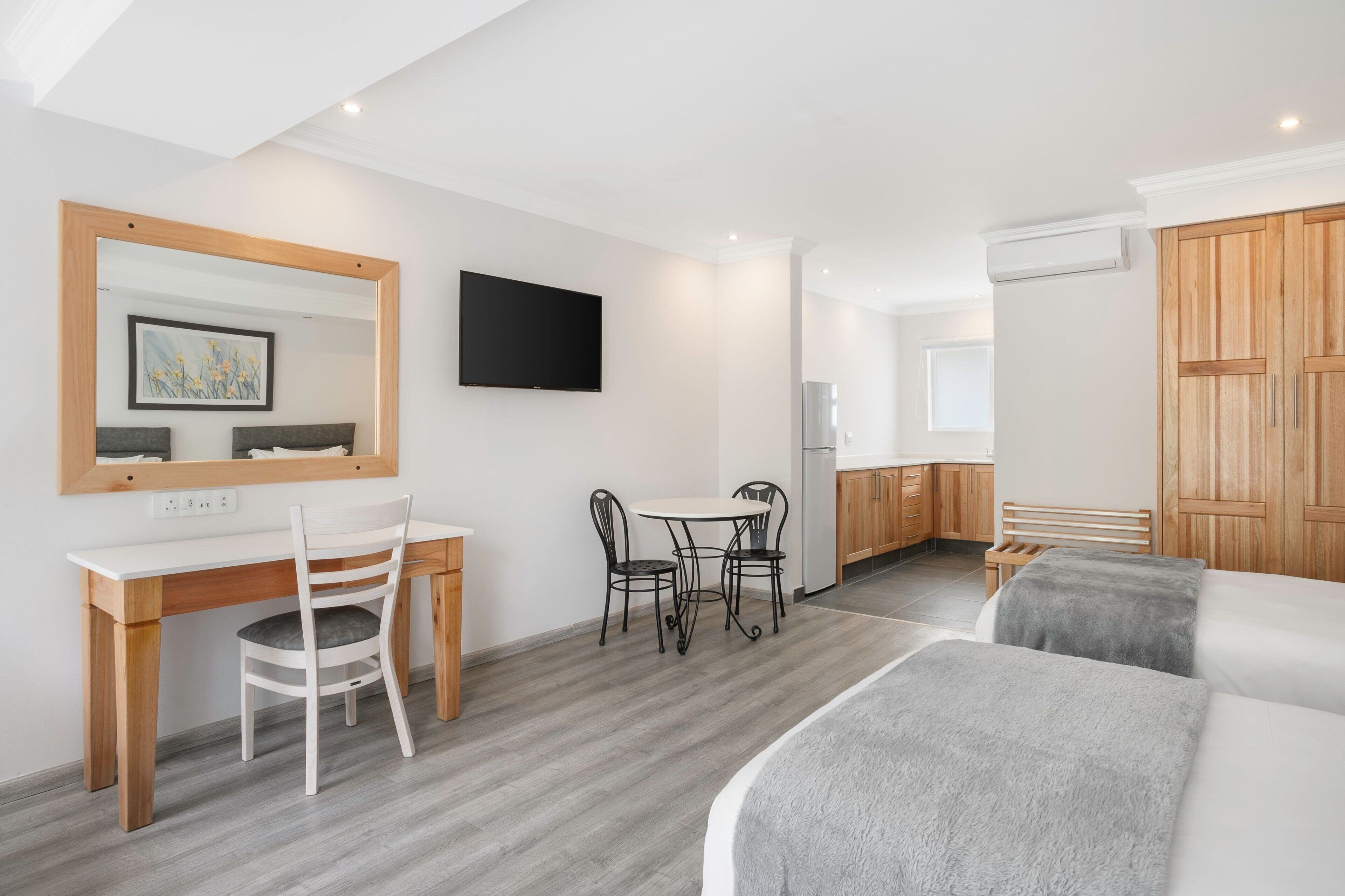 Ein modernes Hotelzimmer mit einem Holzbüro, einem Esstisch, einem Fernseher und einem Bett.