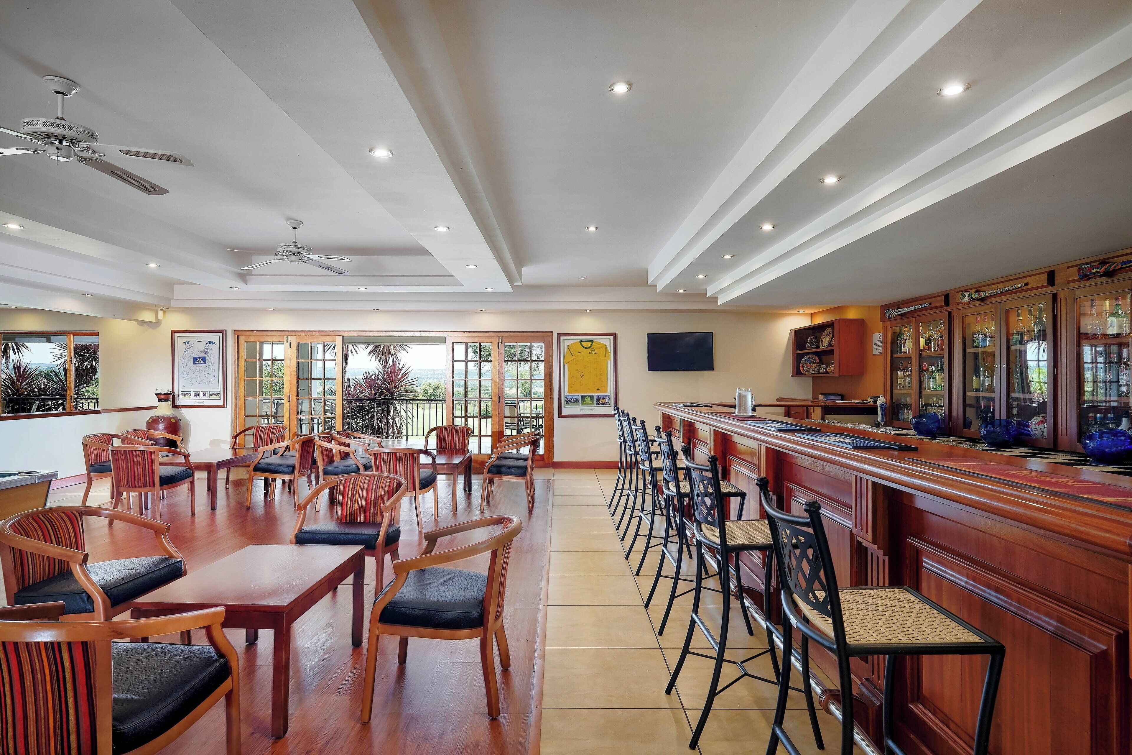Amplio espacio interior con mesas y sillas de madera, una zona de bar con taburetes y ventiladores de techo.
