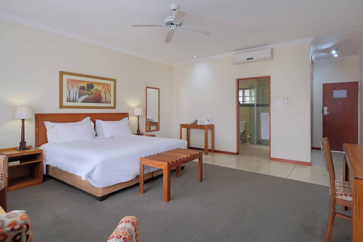 A hotel room with a large bed, bedside tables, a wooden bench, a desk, and a chair.