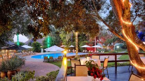 An outdoor dining area with tables set for a meal, surrounded by lush greenery and a pool. - Protea Hotel by Marriott Polokwane Ranch Resort (Polokwane)