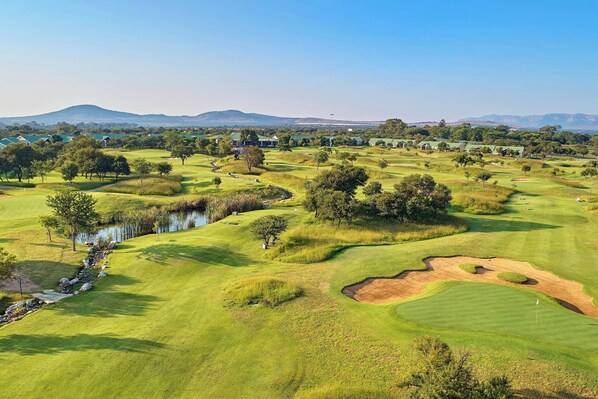 A golf course with bunkers, a water feature, and a mountain in the background.