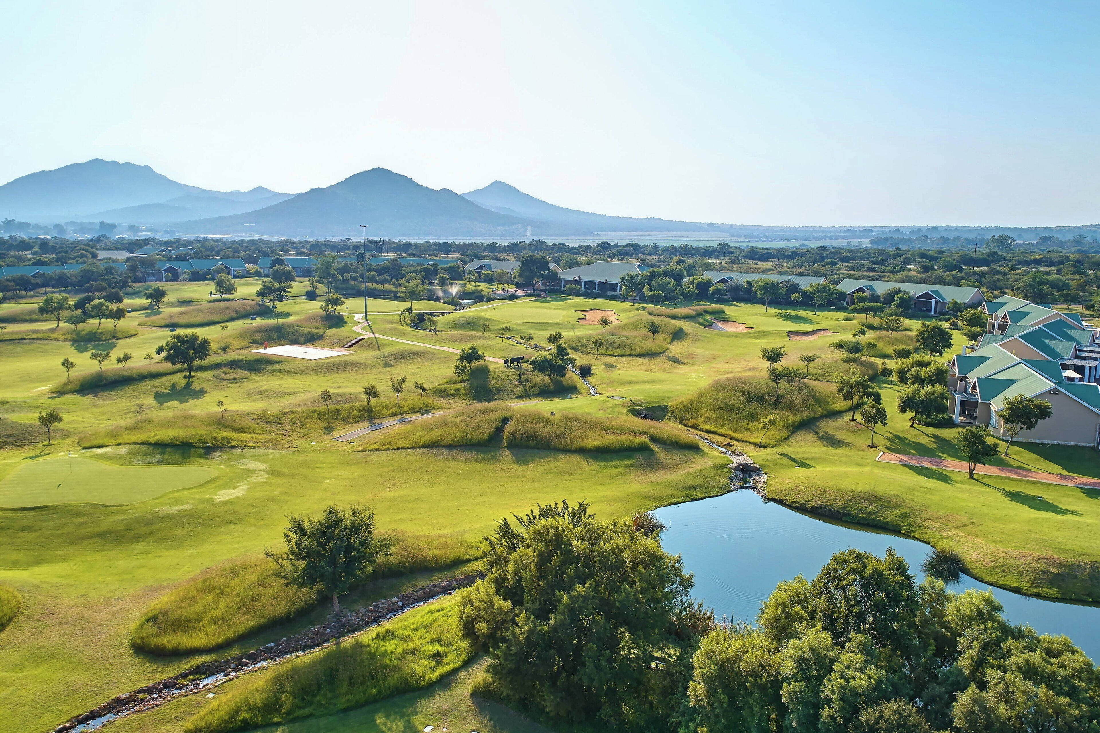 Un campo de golf con un estanque, rodeado de árboles y edificios con tejados verdes.