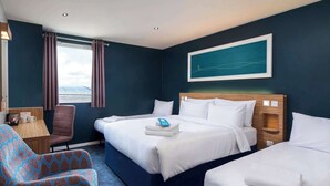 A hotel room with a large bed, two smaller beds, a chair, a desk, and a window with curtains. - Travelodge Edinburgh Central Waterloo Place (Edinburgh)