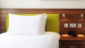 Una habitación de hotel con una cama bien hecha, un cabecero verde y un cuadro colgado en la pared que muestra un campo de golf.