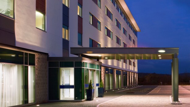 Una entrada de hotel moderna con un vestíbulo cubierto, grandes ventanales y fachada de ladrillo.