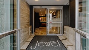 A hotel entrance with a modern design, featuring a glass door, a wooden floor, and a doormat with the hotel's name. - The Jewel Hotel, New York (New York)