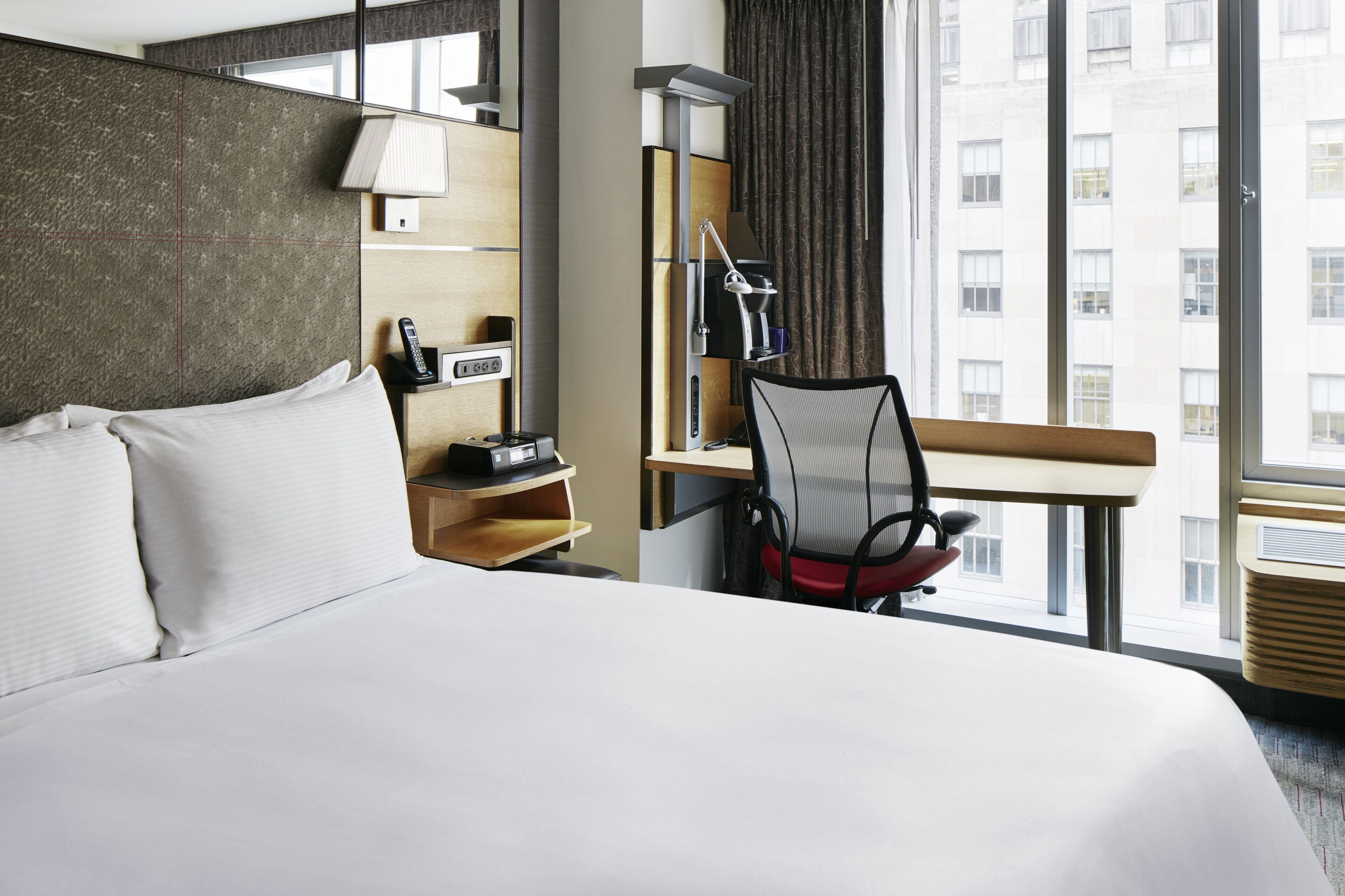 Una habitación de hotel con una cama grande, un escritorio con silla, una lámpara y un teléfono.