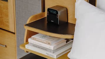 A neatly made bed with a pillow, a bedside table with a digital clock, and a stack of books.