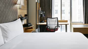 Une chambre d’hôtel avec un grand lit, un bureau avec une chaise, une lampe, un téléphone et une fenêtre avec des rideaux.