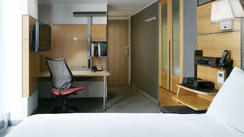 A hotel room with a bed, a desk with a chair, a television, a coffee maker, a phone, and a lamp.