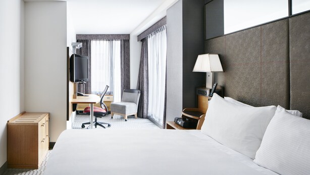 Une chambre d’hôtel avec un grand lit, un bureau avec une chaise, une télévision, une lampe et un téléphone.