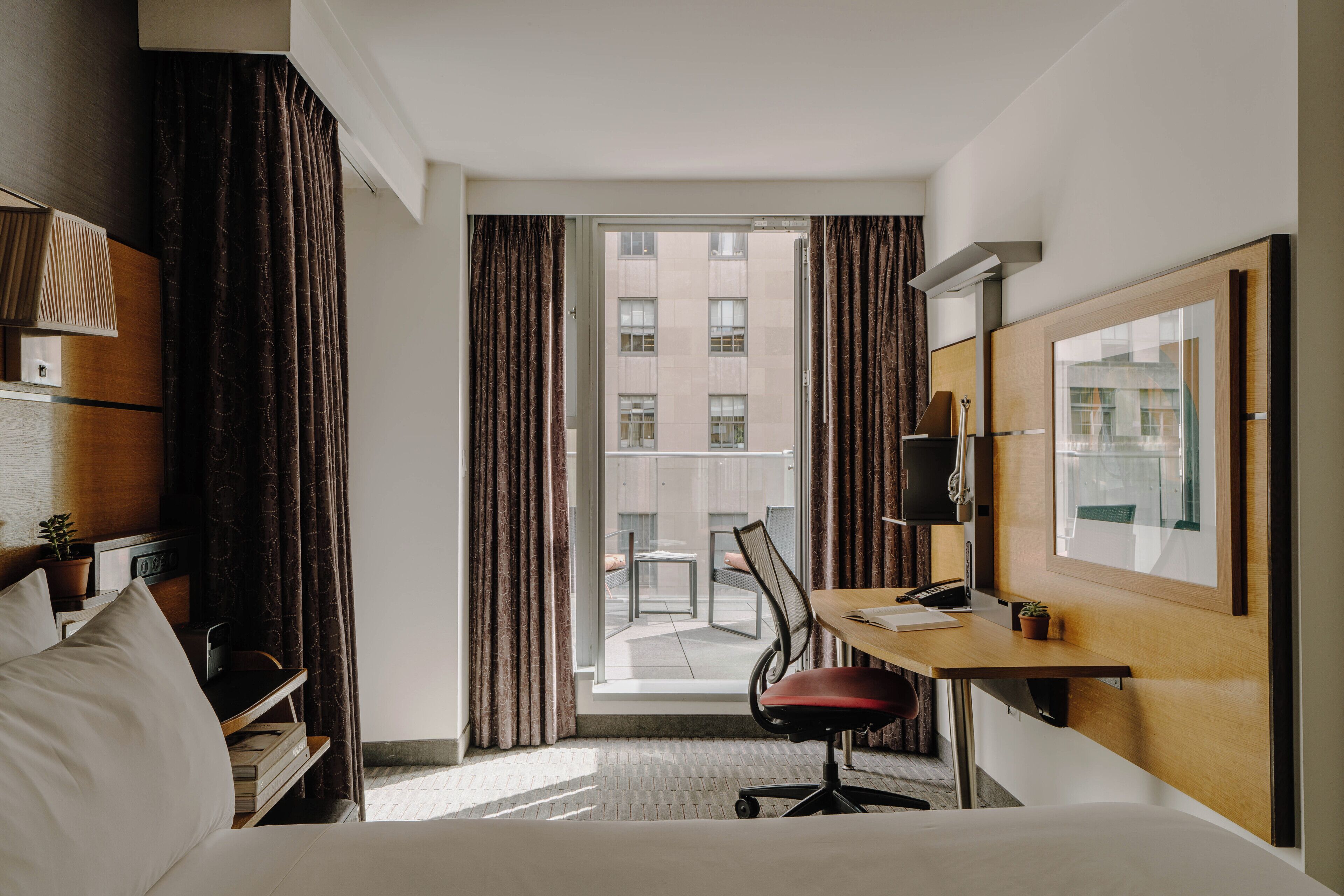Habitación de hotel con cama, escritorio, silla y un amplio ventanal con cortinas.