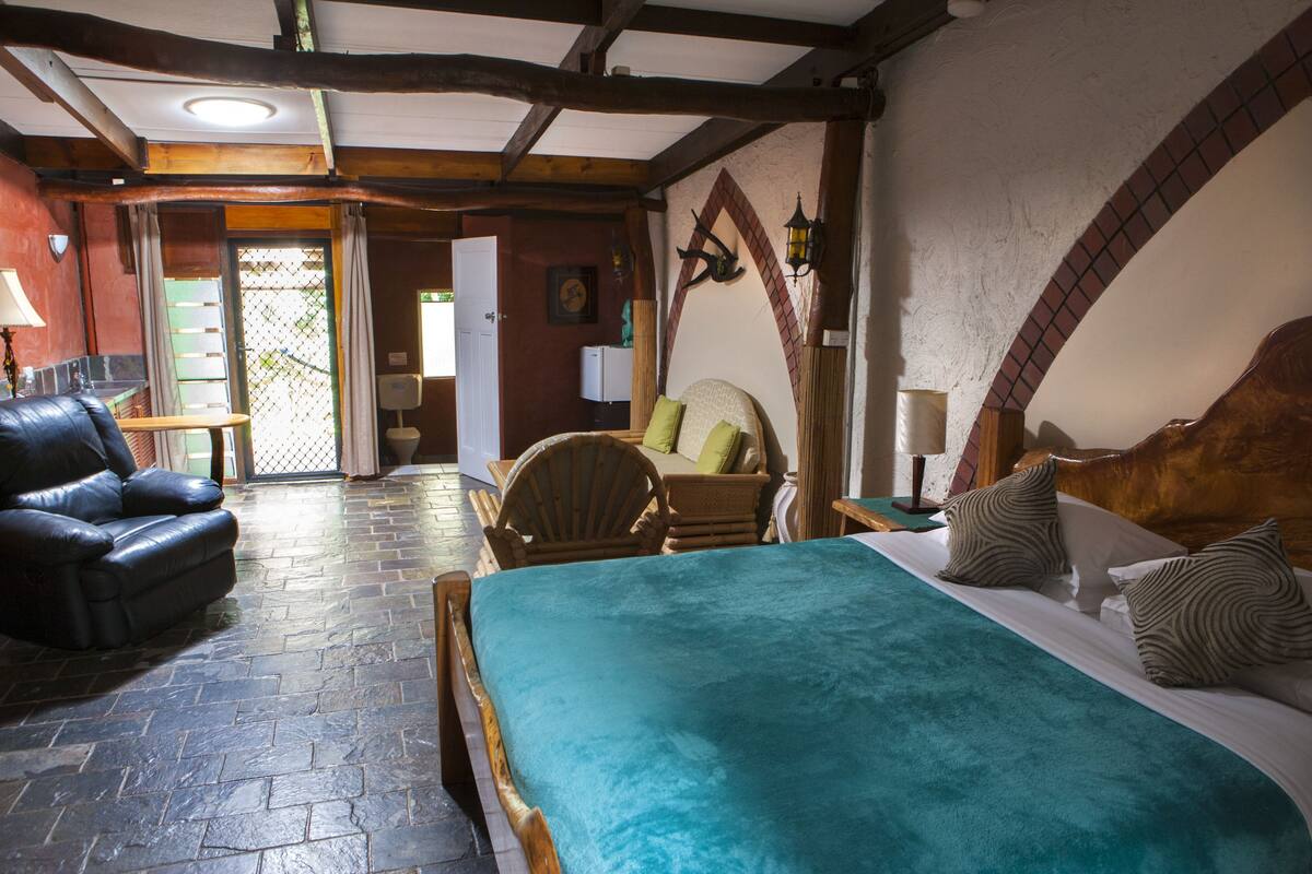 A cozy room with a bed, a leather chair, a wooden table, and a small table with a lamp.