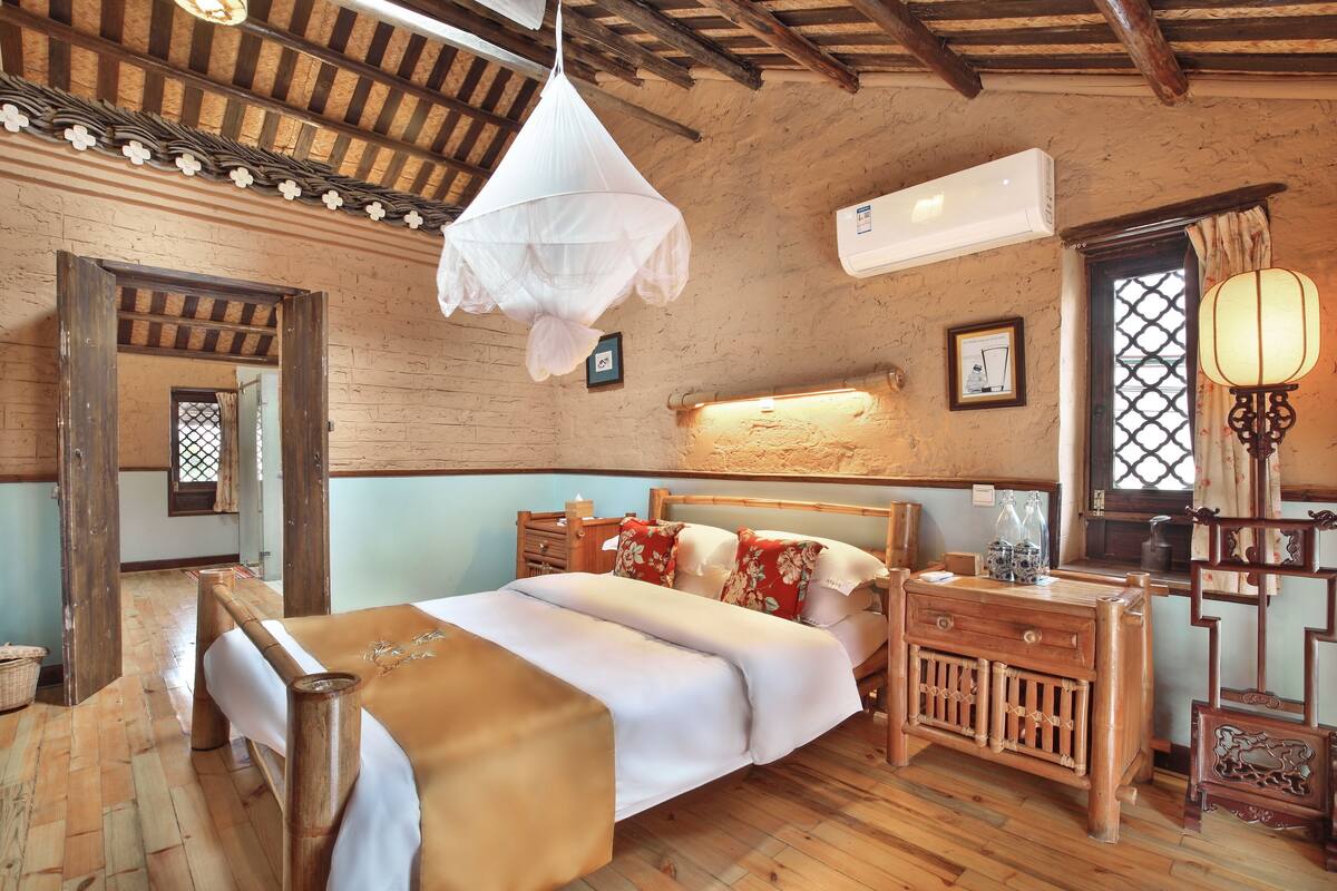 A traditional wooden room with a bed, bedside table, and a hanging mosquito net.