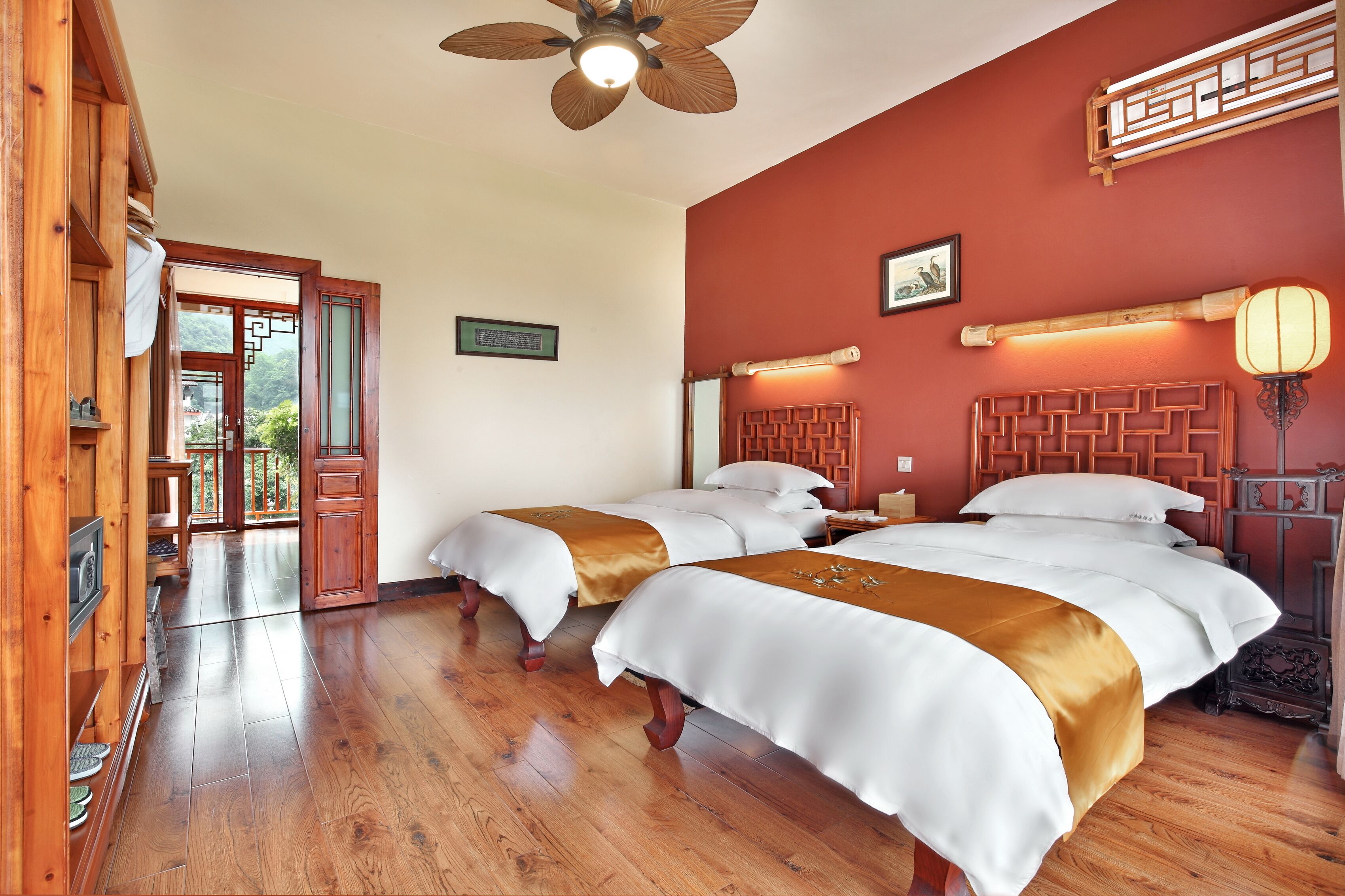A hotel room with two beds, wooden flooring, a ceiling fan, and a view of the outdoors.