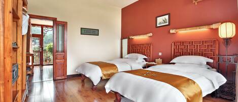 A hotel room with two beds, wooden flooring, a ceiling fan, and a view of the outdoors.