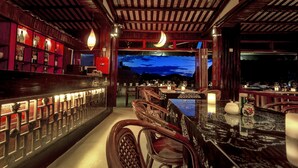 Zona de bar con muebles de madera, vistas al cielo nocturno y una estantería iluminada en rojo con botellas.