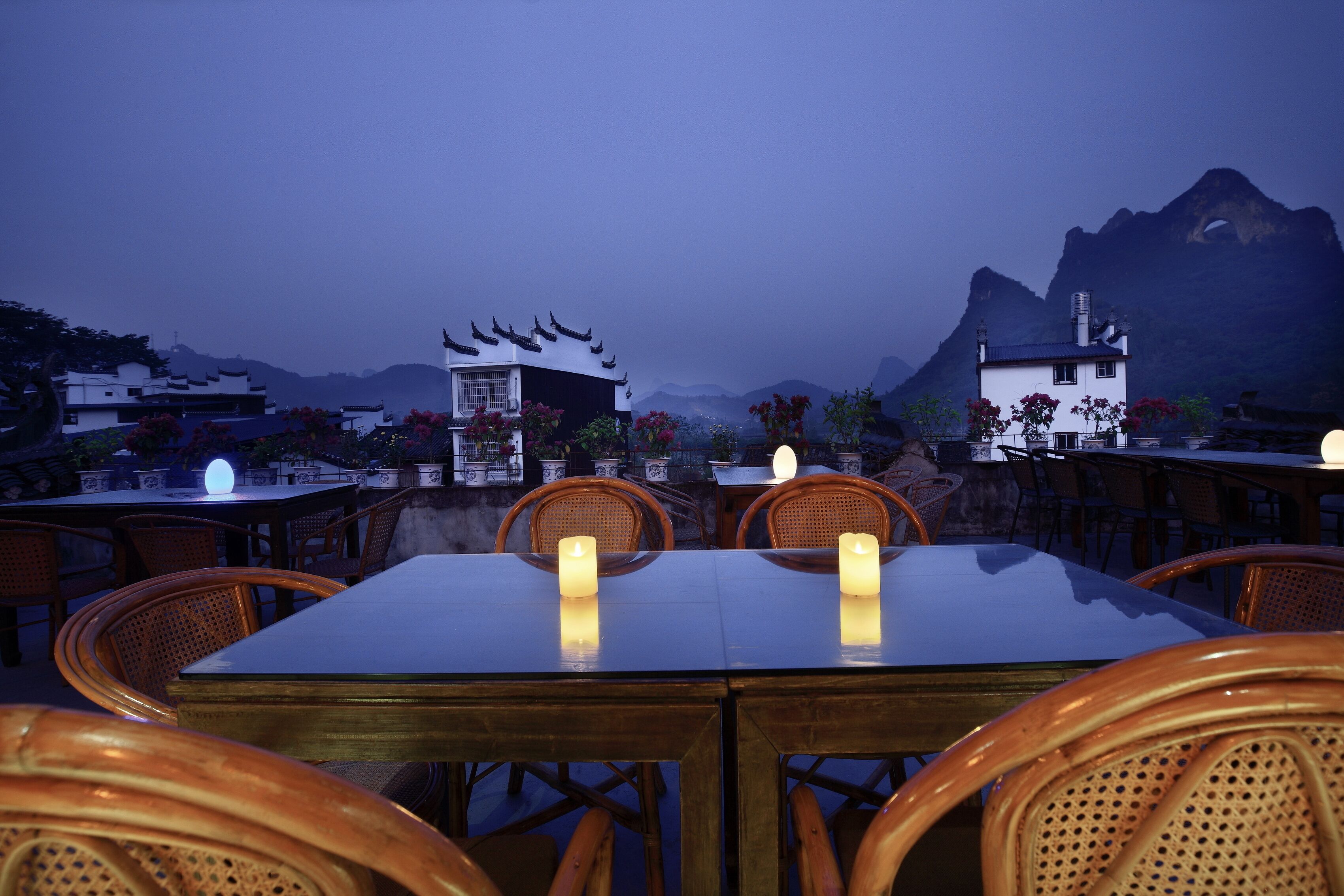 A dining area with tables and chairs, a view of traditional buildings, and a mountain in the background.