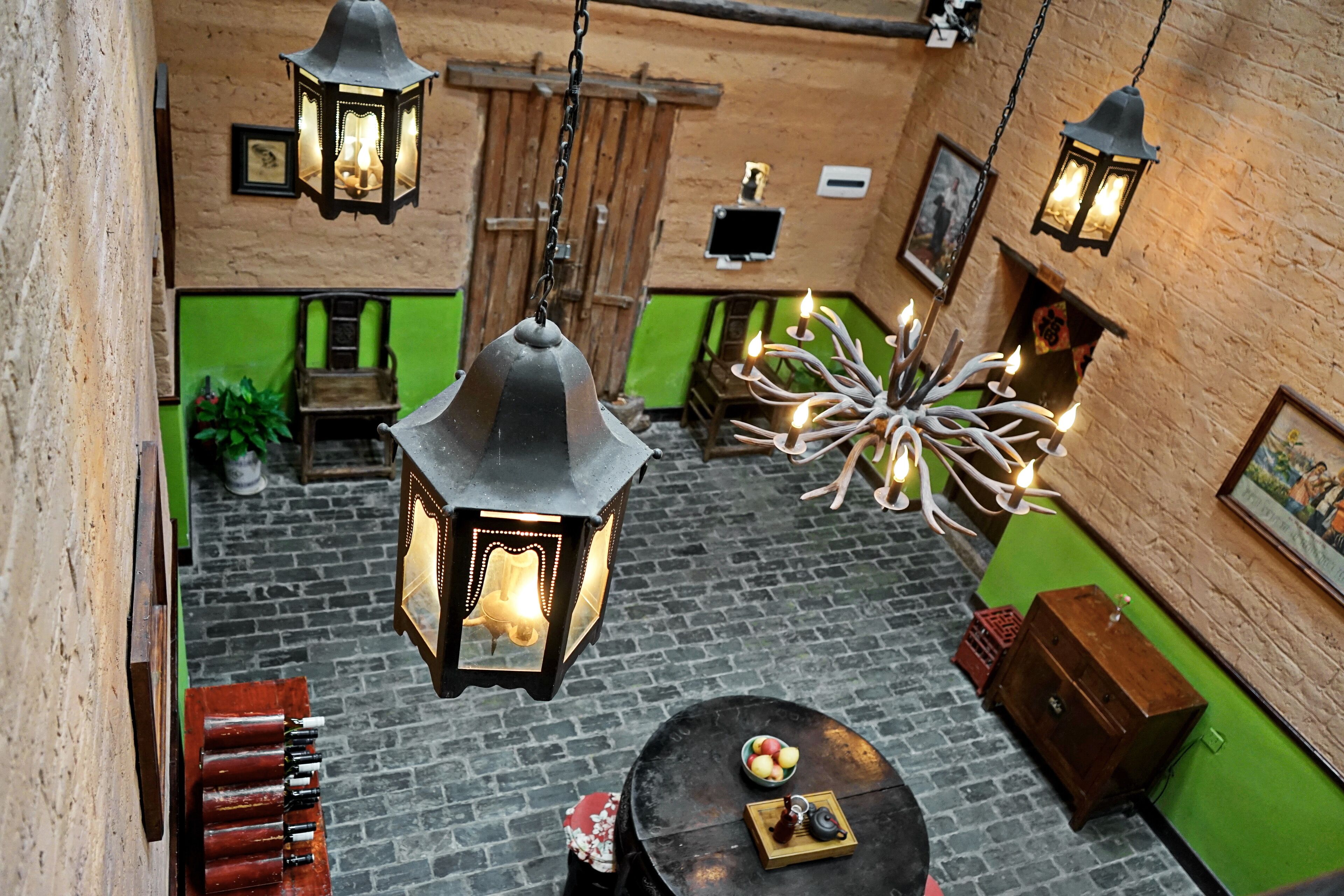 A cozy room with a brick floor, green walls, and hanging lanterns. There is a table with a bowl of fruit and a decorative item.