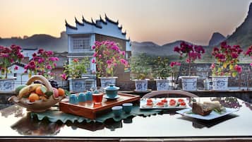 Una mesa dispuesta con fruteros, tetera, tazas y pastelería, con vistas a la arquitectura tradicional y montañas.