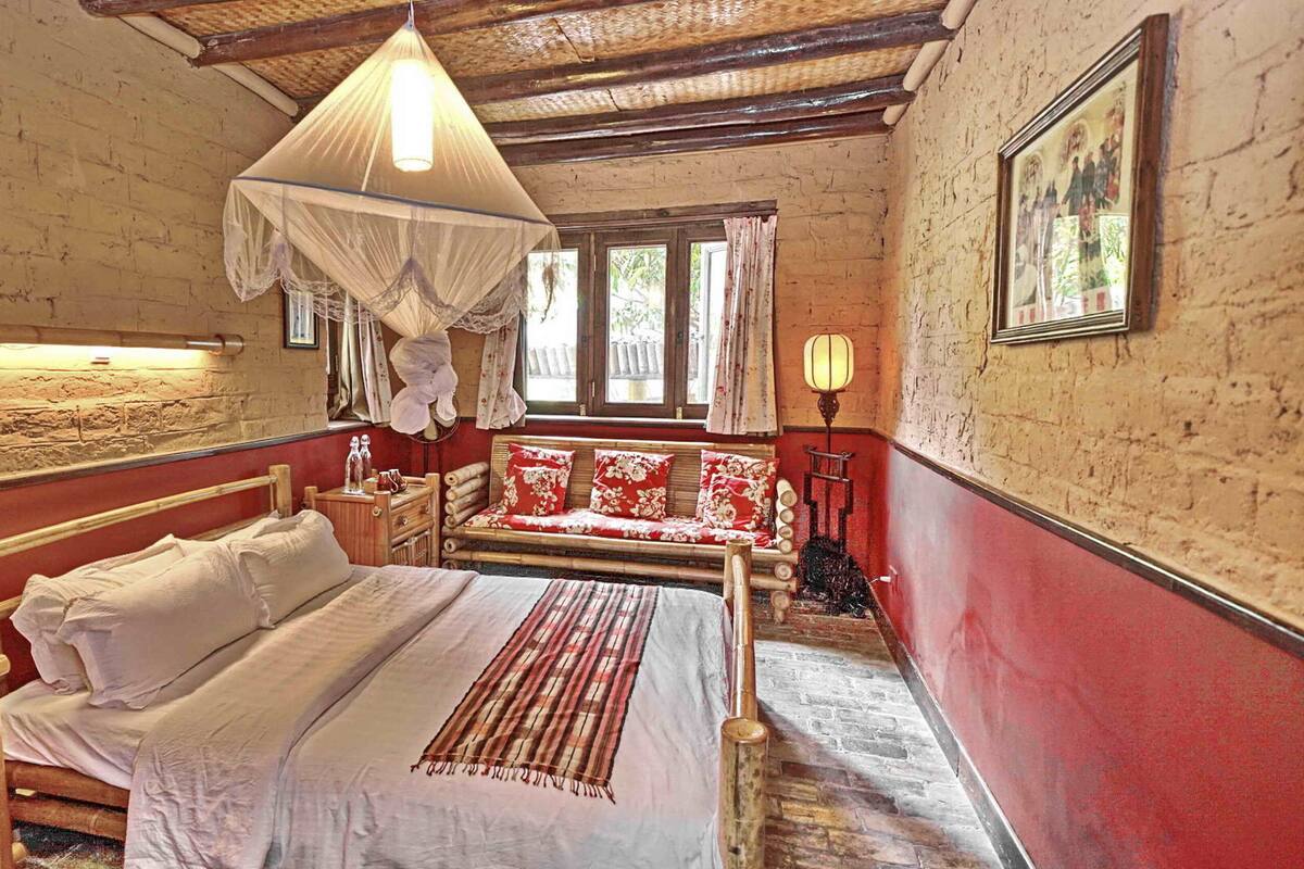 A room with a bed, a bench, a lamp, and a window.