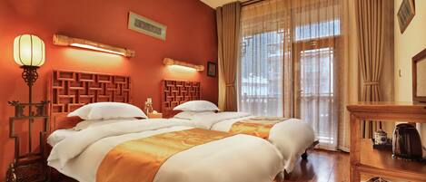 Une chambre d’hôtel avec deux lits, des têtes de lit en bois, un ventilateur de plafond, une table de chevet, une lampe et une vue sur l’extérieur grâce à de grandes fenêtres.