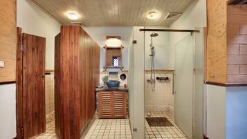 A bathroom with wooden doors, a tiled floor, a shower area, and a small sink with a blue basin.