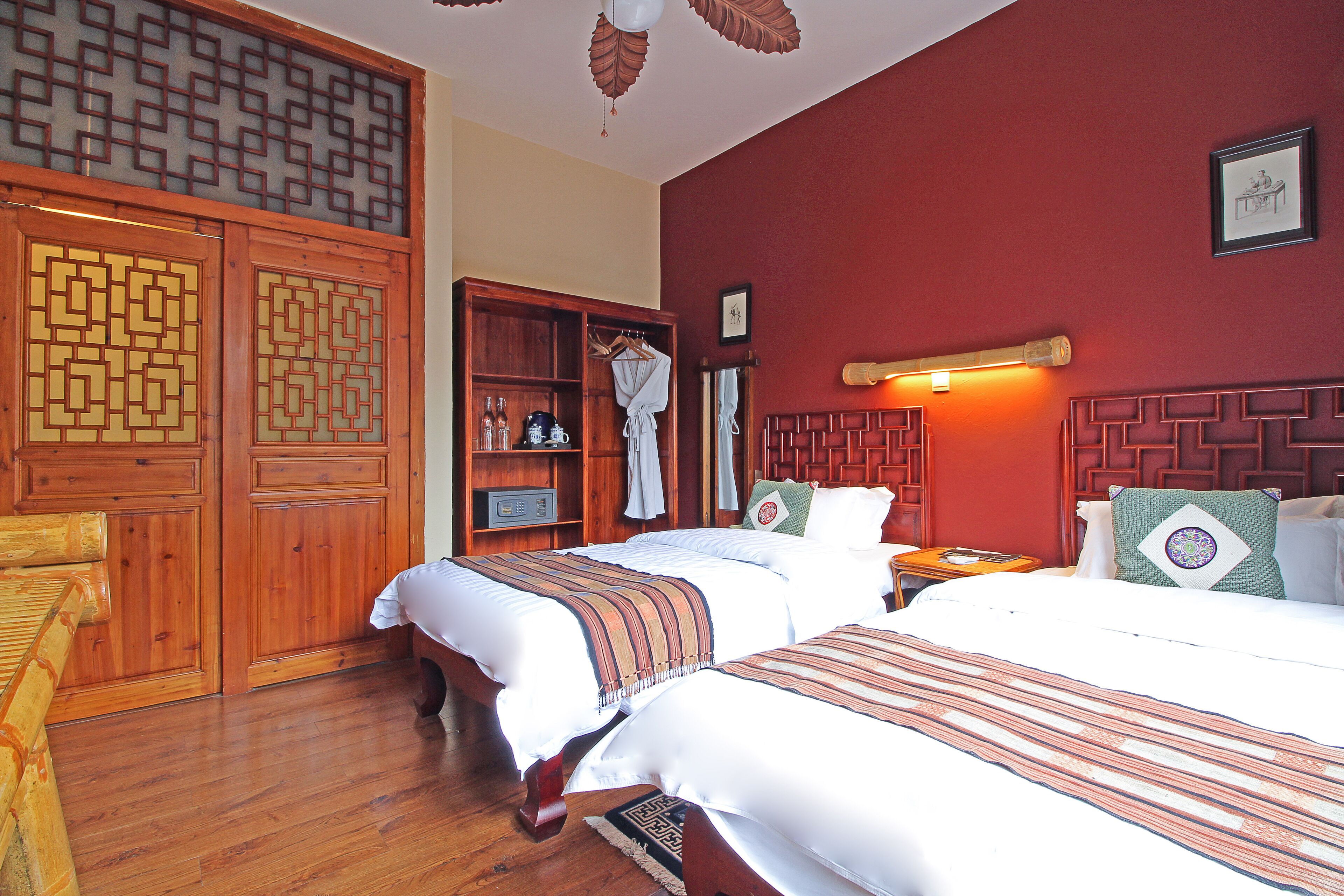 A hotel room with two beds, wooden headboards, a wardrobe, and a shelf with toiletries.