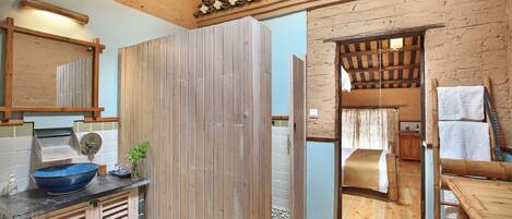 A rustic bathroom with a wooden vanity, a large blue basin, and a wooden shower enclosure.