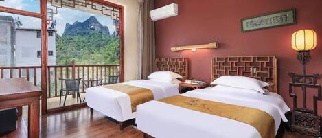 A hotel room with two beds, a balcony with a mountain view, a traditional Chinese wall panel, and a ceiling fan.