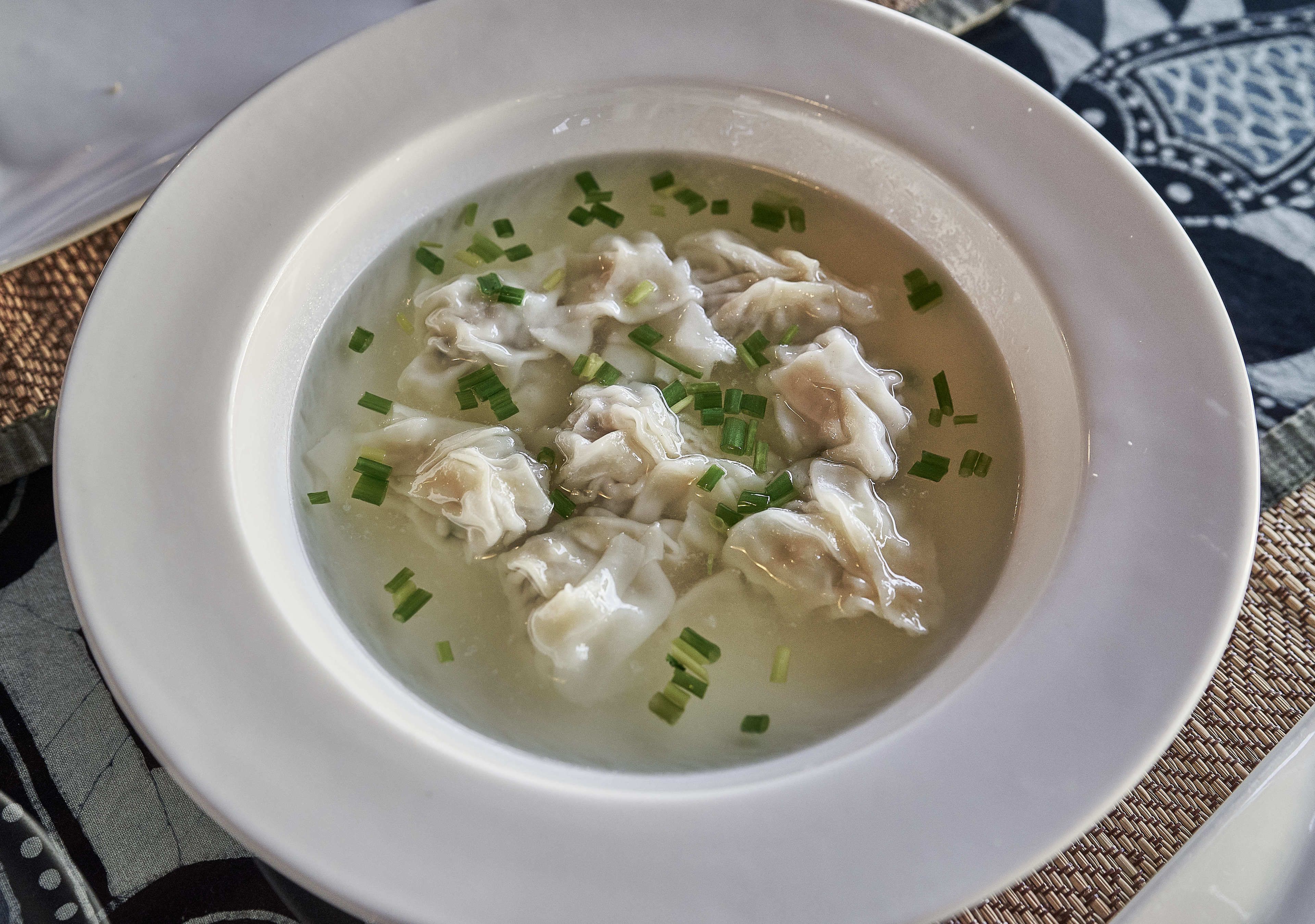 A bowl of soup with dumplings and chopped green onions.